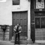 Monochrome image of a man standing by a door on a city street