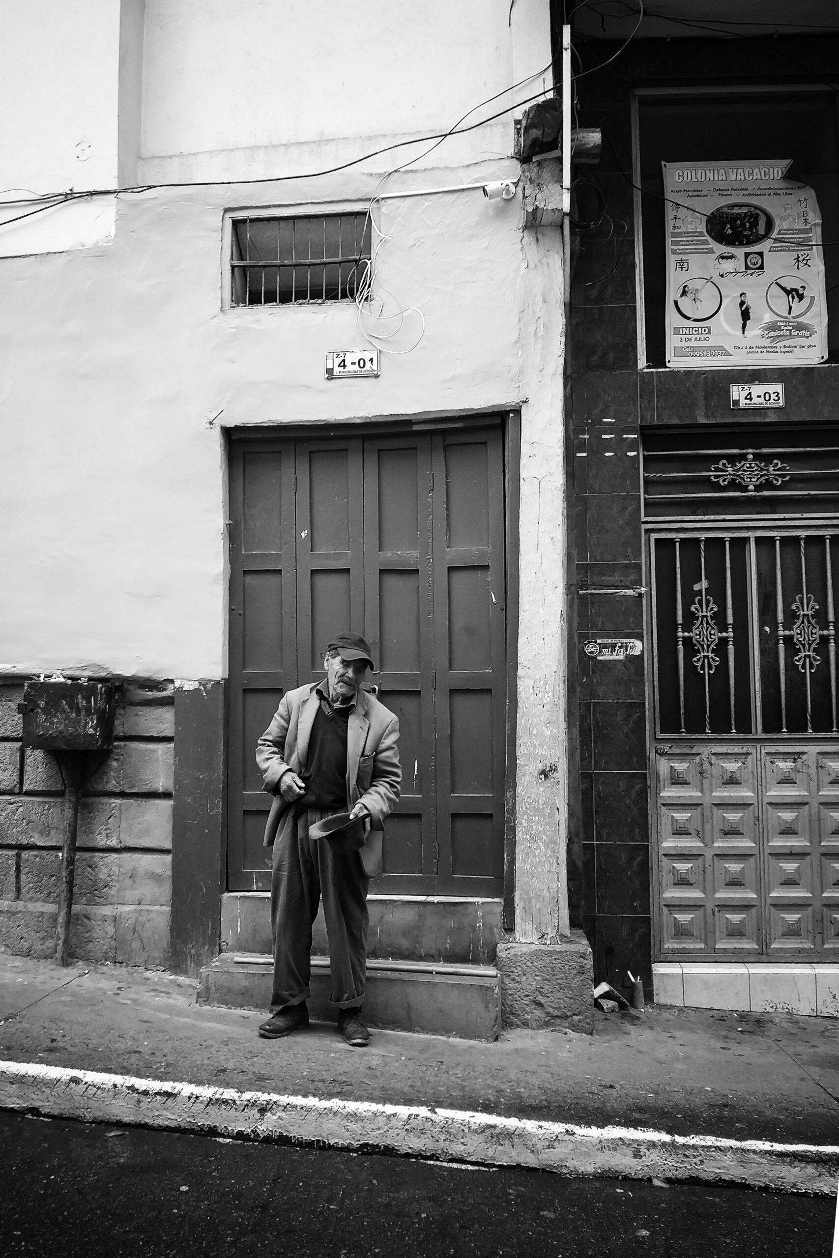 Monochrome image of a man standing by a door on a city street